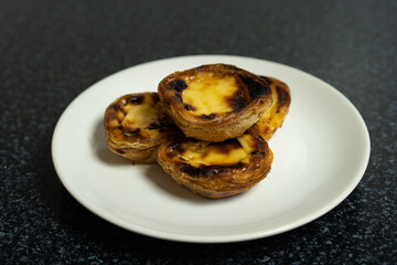 Egg tart, traditional Portuguese dessert, pastel de nata on a parchment paper. Blue background. Top view.
