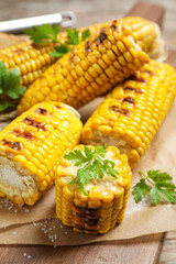 Delicious grilled corn cobs on wooden table, closeup