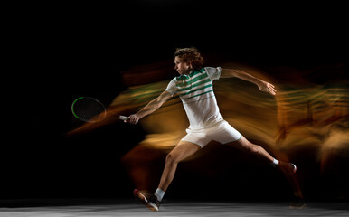 On fire. Young professional sportsman playing tennis isolated on black background in mixed light. Training, practicing in motion, action. Power and energy. Movement, ad, sport, healthy lifestyle
