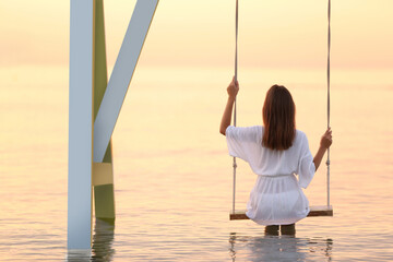 Young woman enjoying sunrise on swing over water