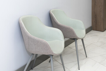 Front view of modern, simple chairs against grey wall in a minimal style, waiting room interior....