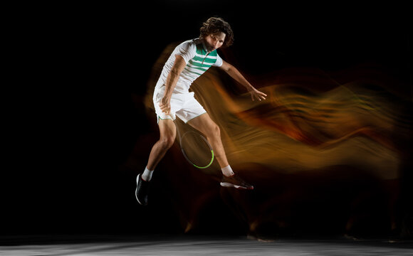 Flying. Young professional sportsman playing tennis isolated on black background in mixed light. Training, practicing in motion, action. Power and energy. Movement, ad, sport, healthy lifestyle © master1305