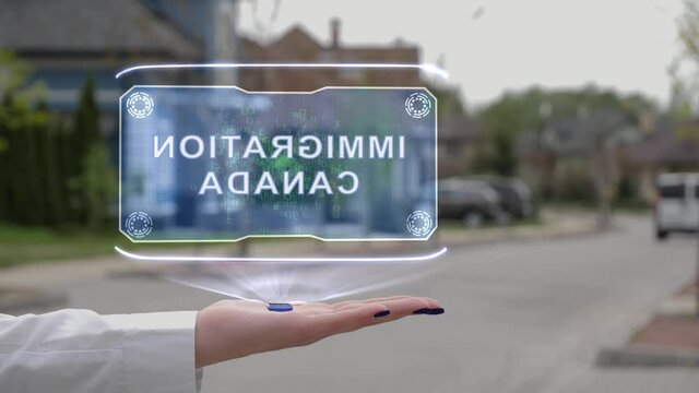 Female hand showing conceptual hologram with text Immigration Canada. Unrecognizable woman in white holds future holographic technology on the background of a street with private houses