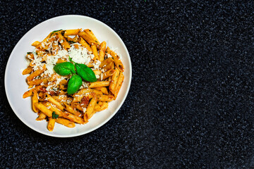 Penne pasta amatriciana in tomato sauce and cheese decorated with basil, top view.
