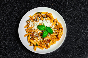 Penne pasta amatriciana in tomato sauce and cheese decorated with basil, top view.
