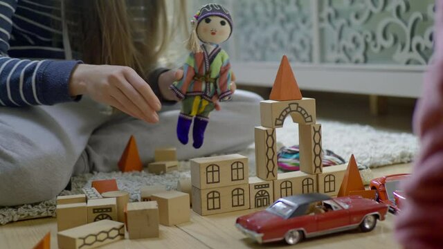 Woman hands playing with toy blocks and a doll, showing kid how to build. Mother and child playing together. Doll wears national costume.Retro car model near blocks. Domestic interior.A day in a life.