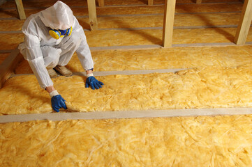 Man installing thermal insulation layer under the roof - obrazy, fototapety, plakaty