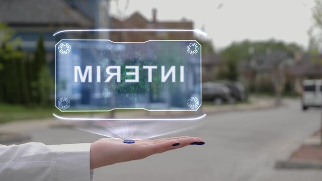 Female hand showing conceptual hologram with text INTERIM. Unrecognizable woman in white holds future holographic technology on the background of a street with private houses
