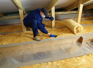 Worker thermally insulating house attic with glass wool