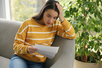 Worried woman reading letter on sofa at home