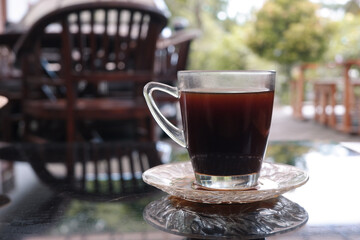 A glass of black coffee on a glass table with a blurred background 