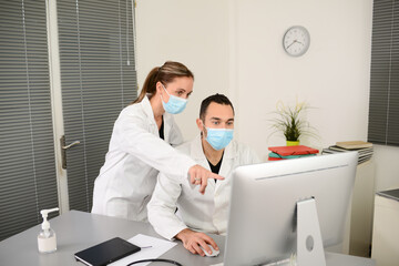 group of two medical professional male and female doctor wearing surgical mask in a hospital office desk with computer