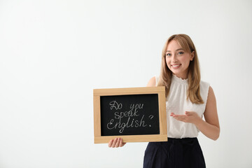 Young female teacher holding chalkboard with words DO YOU SPEAK ENGLISH? on light background. Space for text