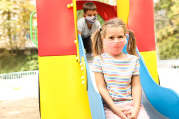 Fototapeta na wymiar Little children with medical face masks on playground during covid-19 quarantine