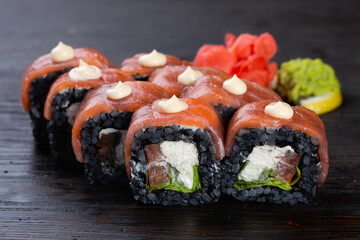 .traditional black Japanese sushi with salmon and soft cheese, cucumber and red caviar, garnished with sauce and white sesame seeds. Japanese kitchen. Japanese restaurant.