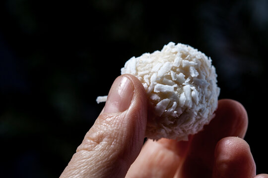 Coconut balls, ehite chocolate rafaello candies. Vegetarian round tasty dessert, hand holding a ball