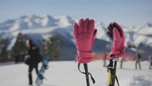 Women's ski gloves worn on poles stuck in the snow at a ski resort.