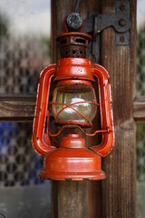 Stara czerwona oliwna lampa zawieszona na drewnianym oknie starego domu