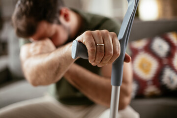 Young man with a hand on his crutches sitting on sofa. Man having back pain.