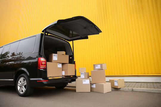 Black delivery van and many different parcels near yellow building outdoors. Courier service