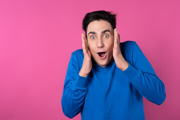 The young man is surprised. Pink background. Blue clothes.