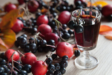 Homemade tincture of black chokeberry and red apples. An autumn composition of berries of mountain ash and small apples. Granen Wineglass
 with home-made alcohol.