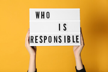 Woman holding light box with phrase Who Is Responsible on orange background, closeup