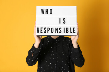 Woman holding light box with phrase Who Is Responsible on orange background