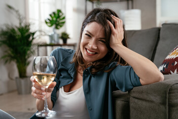 Happy woman sitting on the floor, drinking wine. Smiling woman celebrate with wine at home..