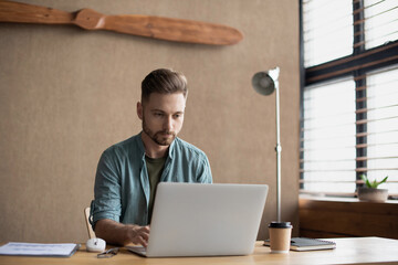 Fototapeta premium Young handsome man using laptop at modern office, Businessman or student working online on computer, Freelance, online marketing, distance education, e-learning, home work and lockdown concept.