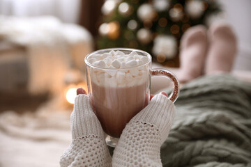 Woman with delicious hot drink wrapped in plaid at home, closeup