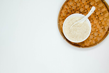 A white ceramic bowl and spoon and of long grain white rice, on rattan handmade bowl isolated on white background. Copy space
