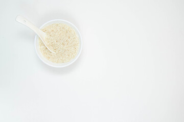 A white ceramic bowl and spoon and of long grain white rice, isolated on white background. Copy space