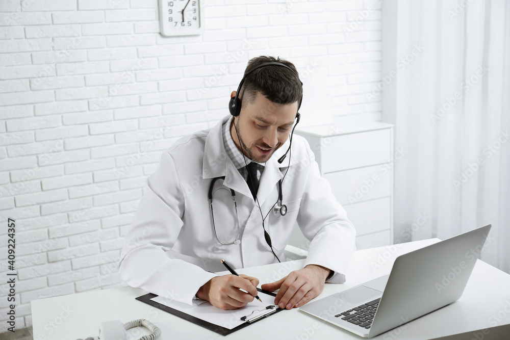 Wall mural Doctor with headset consulting patient online at desk in clinic. Health service hotline