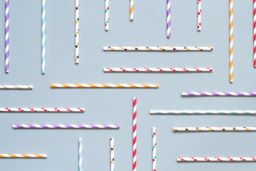 Striped and dotted paper drinking straws on grey background top view
