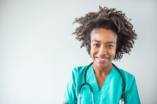 African American medical professional. Friendly nurse with stethoscope isolated on grey. Smiling female healthcare professional looks at the camera while in hospital hallway. 