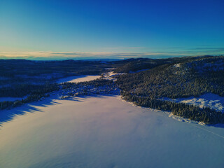Frozen lake in the Norwegian wilderness, covered in undisturbed snow on a bright sunny day. Aerial photo.