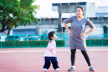 Fototapeta premium Mother and daughter are exercising. Cute girl laughed happily and looked at her mom. The mother made a irksome face be merciful for the little child. The family enjoyed the evening sport activities.