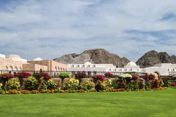 Beautiful green grass and colorful flowers in the garden in front of the gate that surrounds the buildings that form Al Alam Palace complex. Muscat, Oman.