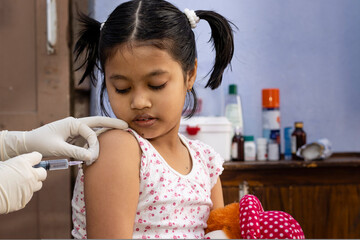 an Indian girl child with doll in hand looks on during vaccination