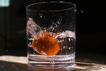 Close up shoot of mandarin orange making a splash into water in a crystal glass. The morning rays makes it look more beautiful.