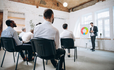 Attention. Male speaker giving presentation in hall at university workshop. Audience or conference hall. Rear view of unrecognized participants. Scientific, business event, training. Education