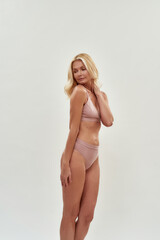 Fototapeta premium Feeling gorgeous at any age. Vertical shot of a sensual middle aged caucasian blonde woman wearing lingerie looking away while posing isolated over grey background