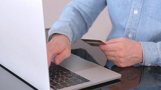 Male hands of cardholder holding credit card making e bank online payment. Man paying for purchase in web store using laptop technology. E Commerce website payments concept. Close up view