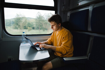 A freelancer man sitting in a train at a table and working on a laptop with a serious face....