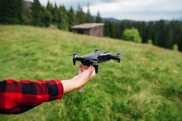 Hand with a drone on a background of mountain views with a meadow and coniferous forest. The pilot...