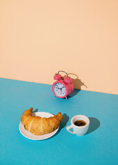 Morning meal, coffee, pastries, alarm clock on a two-tone stylish background