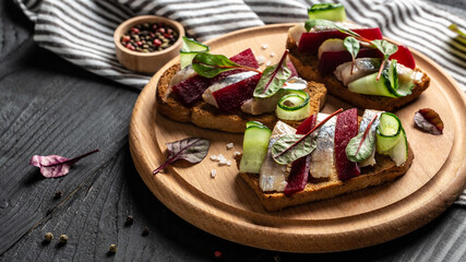 Herring fillet. Sandwich with salted herring, slice beetroot, green cucumber, onion and microgreen on the toasts. Scandinavian cuisine. Tradition Danish open sandwich. top view