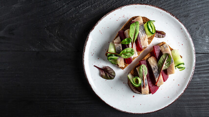 Herring fillet. Sandwich with salted herring, slice beetroot, green cucumber, onion and microgreen on the toasts. Scandinavian cuisine. Tradition Danish open sandwich. top view