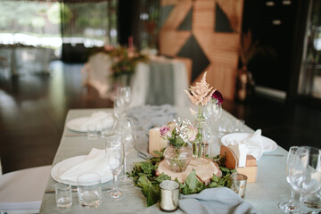 Vintage wedding decor. Beautiful event venue. Creative decoration. Hall decoration. Festive table decor. Stylish stone tablet with table number in grey, green branches and peonies, candles in gold can